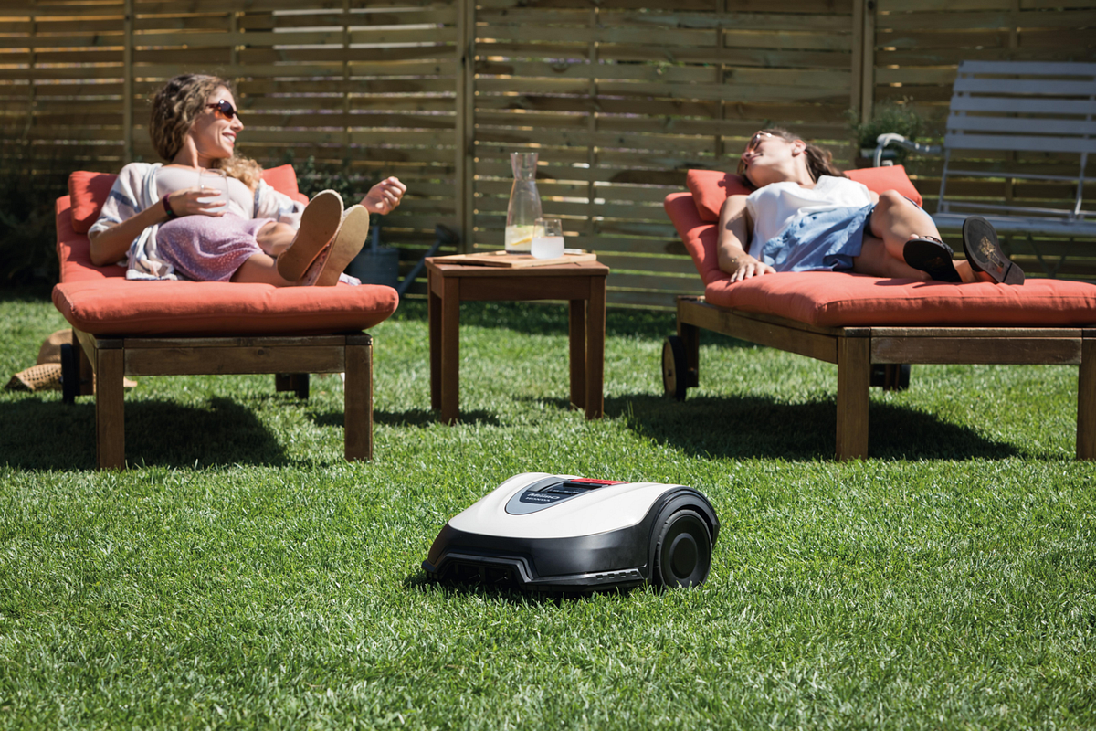 Rasenmähroboter und zwei Frauen auf Gartenliegen
