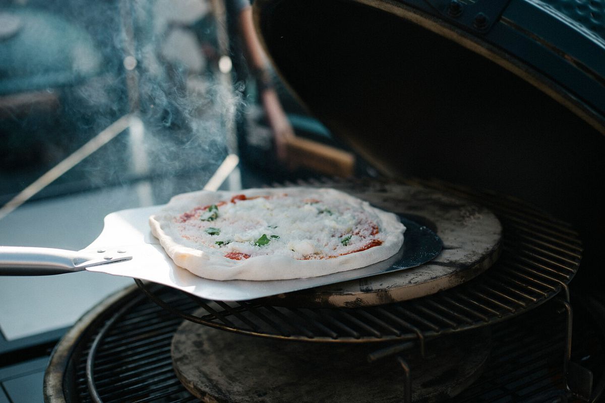 Die fertig belegte Pizza wird mit der Pizzaschaufel auf den Pizzastein gelegt